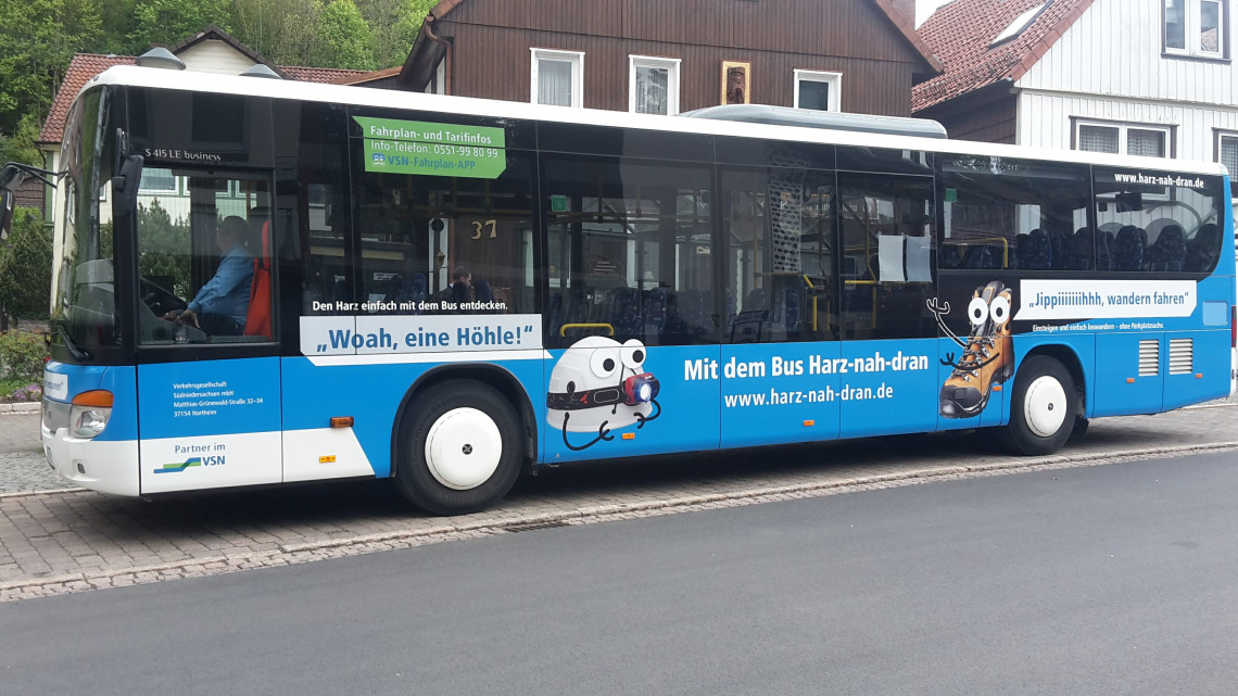Blauer Bus mit Werbeaufdrucken zum Wandern im Harz und einer Höhle hält an der Haltestelle Bad Grund Gesundheitszentrum