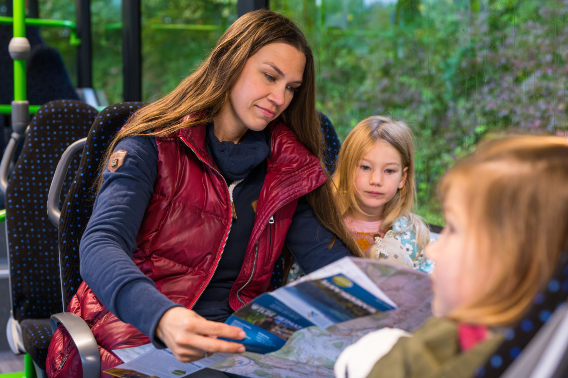 Frau mit zwei Kindern sitzen im Bus und schauen sich eine Karte an.