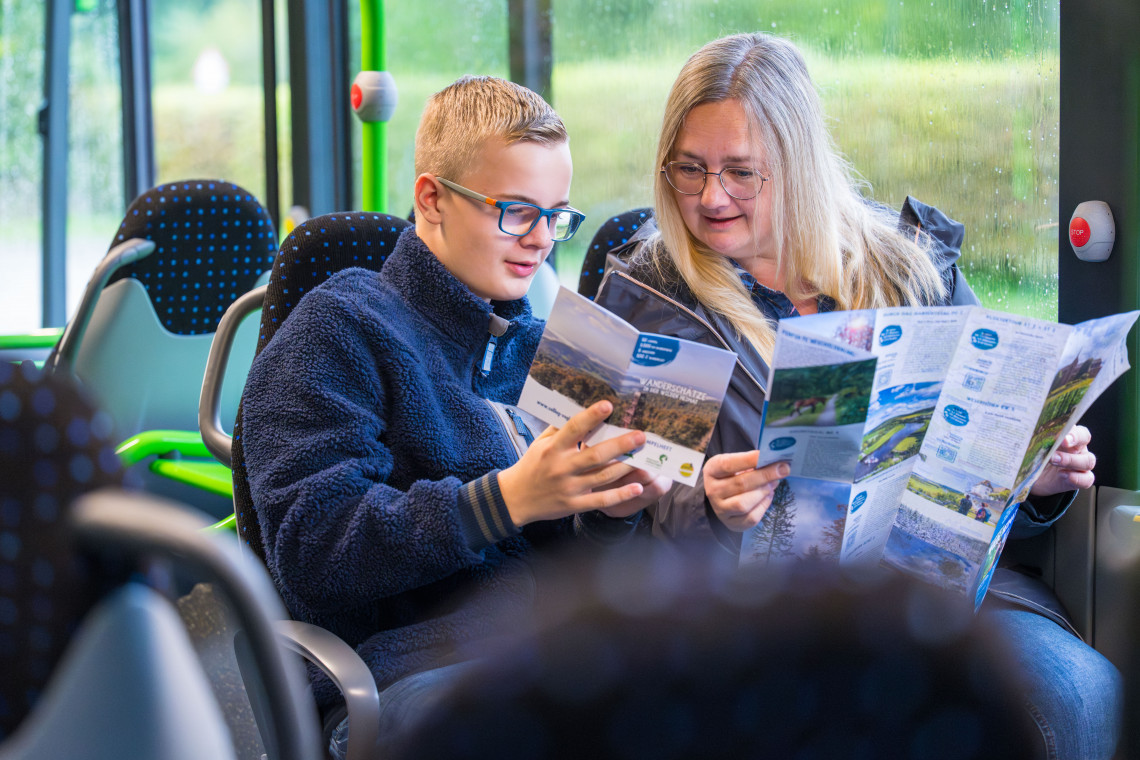 Frau und Jugendlicher sitzen im Bus und schauen Urlaubsprospekte an.