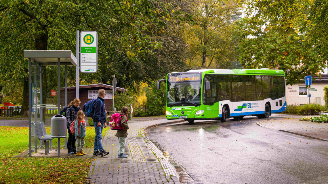 Vier Schulkinder warten an der Haltestelle Neuhaus Schule auf den herannahenden Bus der Linie 510 mit Fahrtziel Holzminden