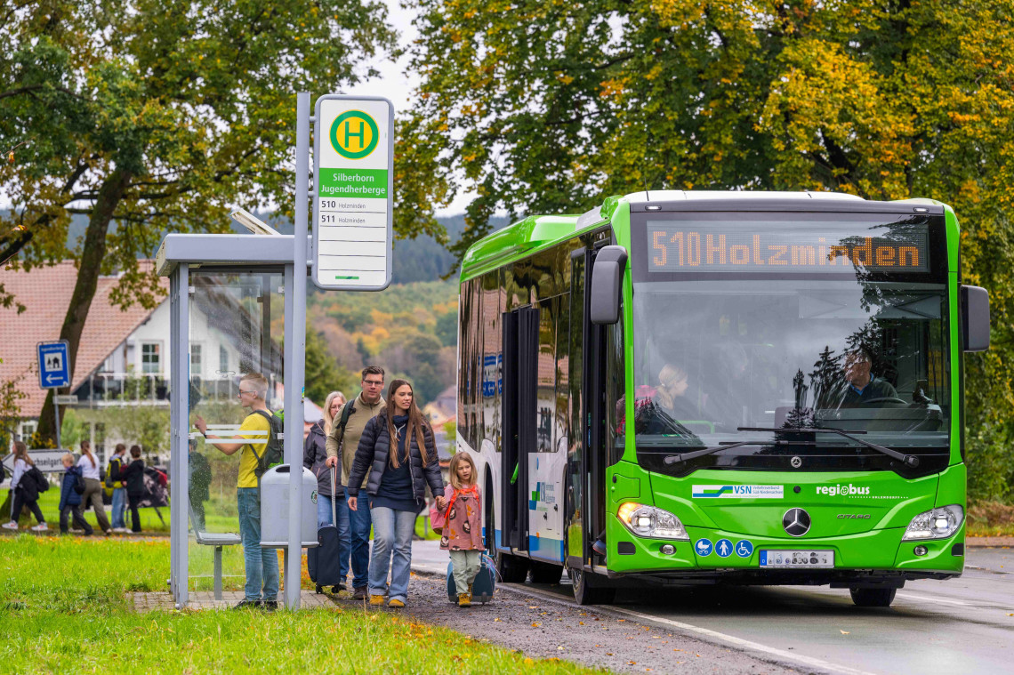 Zwei Frauen, ein Kiind und ein Mann gehen zum Linienbus der Linie 510 Holzminden, der an einer Haltestelle hält.