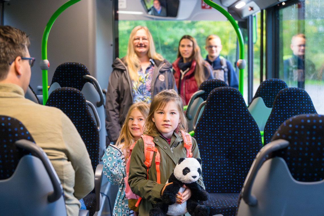 Zwei Kinder mit Rucksäcken steigen mit Erwachsenen in einen modernen Bus